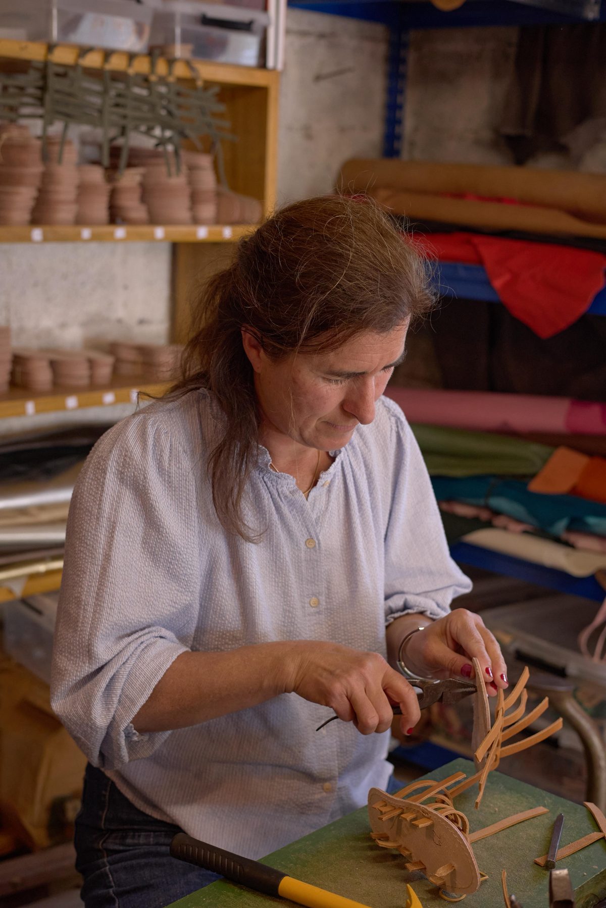 Anne tressant à la main les lanières de cuir dans l'atelier
